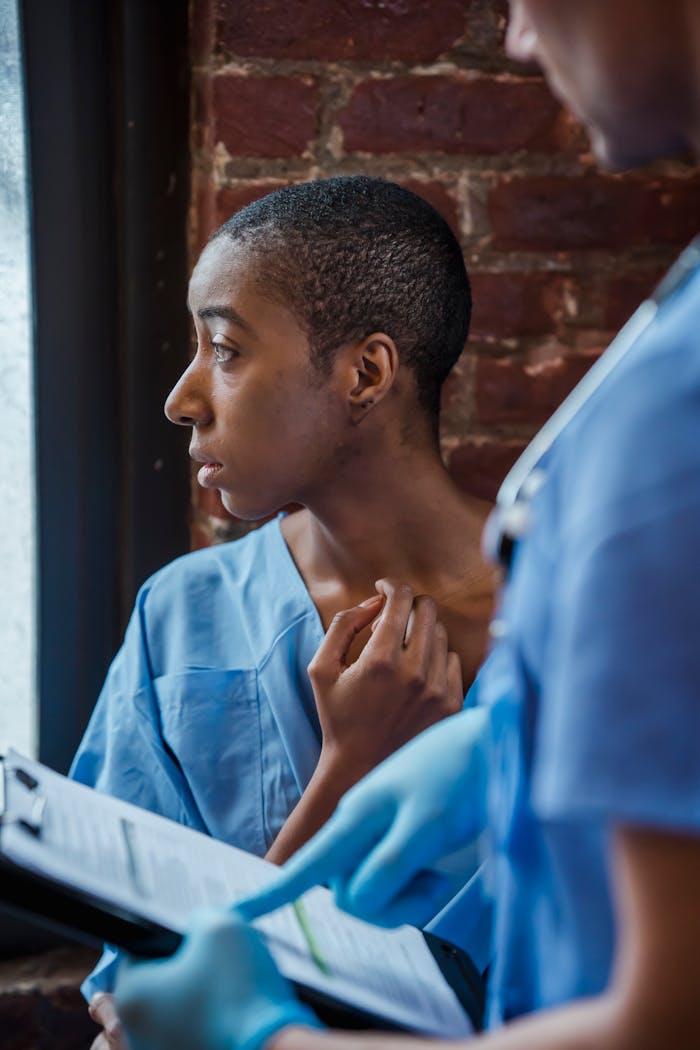 about-us Crop unrecognizable nurse in medical uniform standing with clipboard with diagnosis near thoughtful African American patient in hallway of hospital in daytime