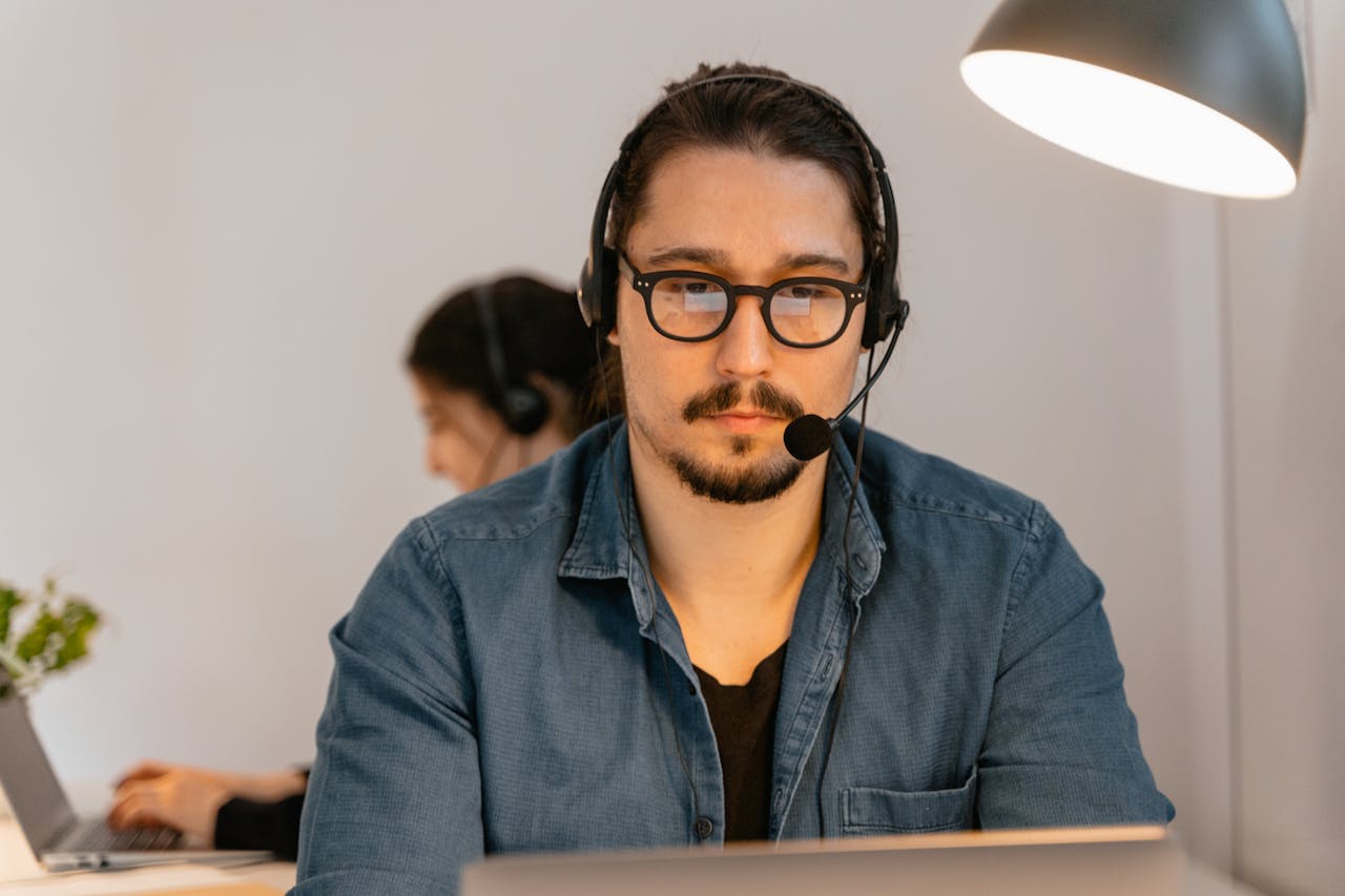services-02 A call center agent wearing headphones, working intently at his desk in a modern office environment.