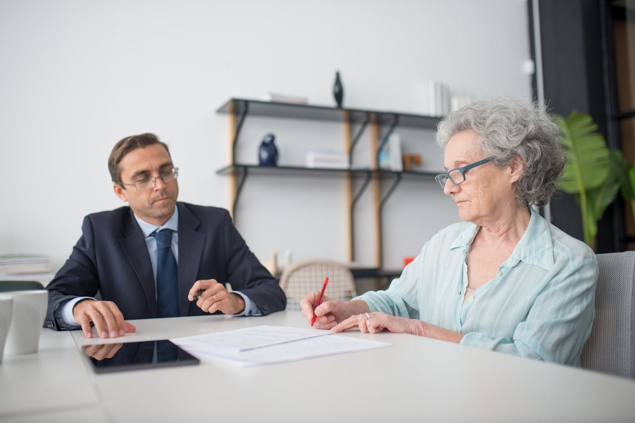 our-story Elderly woman signing paperwork in modern office with consultant.